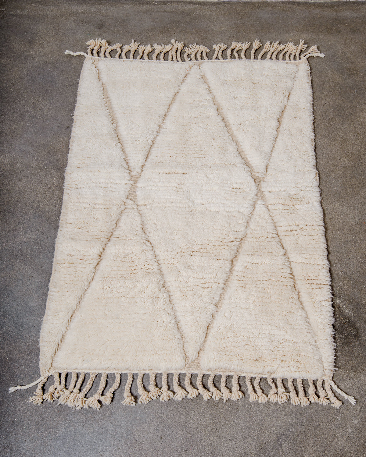 Beniourain rug in cream wool laying on concrete studio floor.